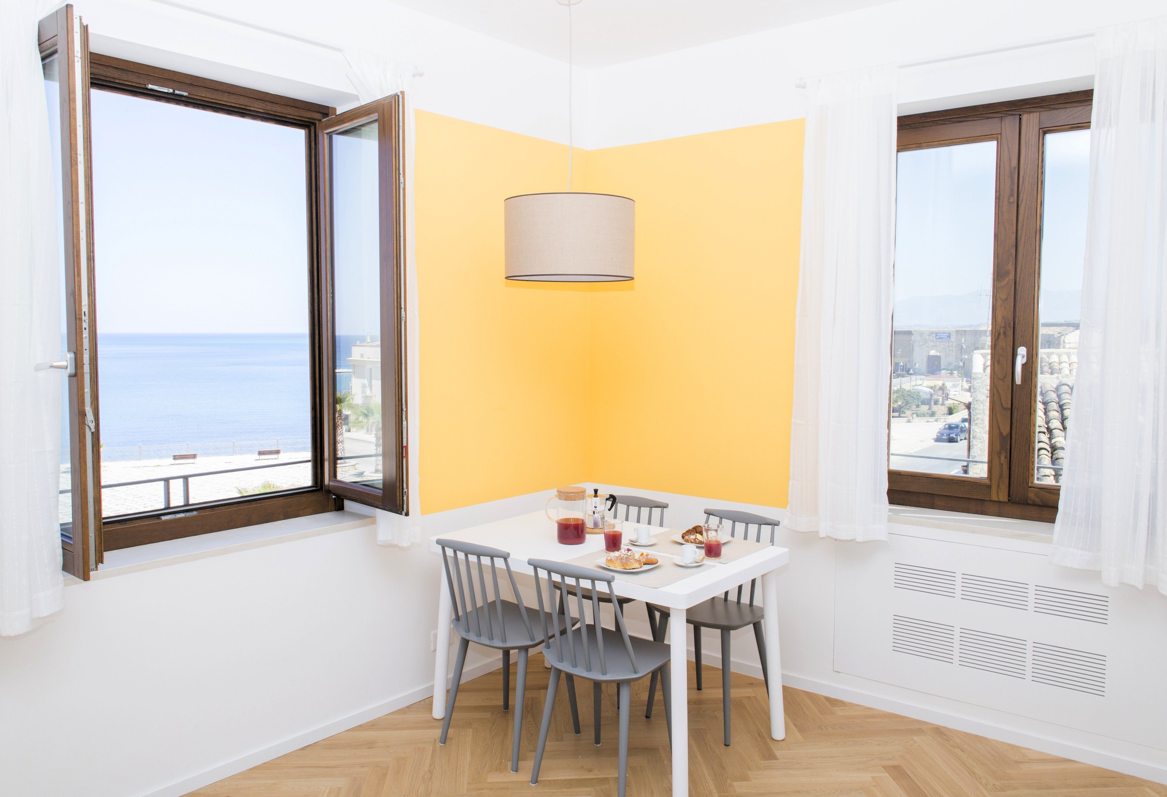 En matplats med ett bord dukat för två personer, utsikt över havet genom ett fönster och en gul accentvägg.