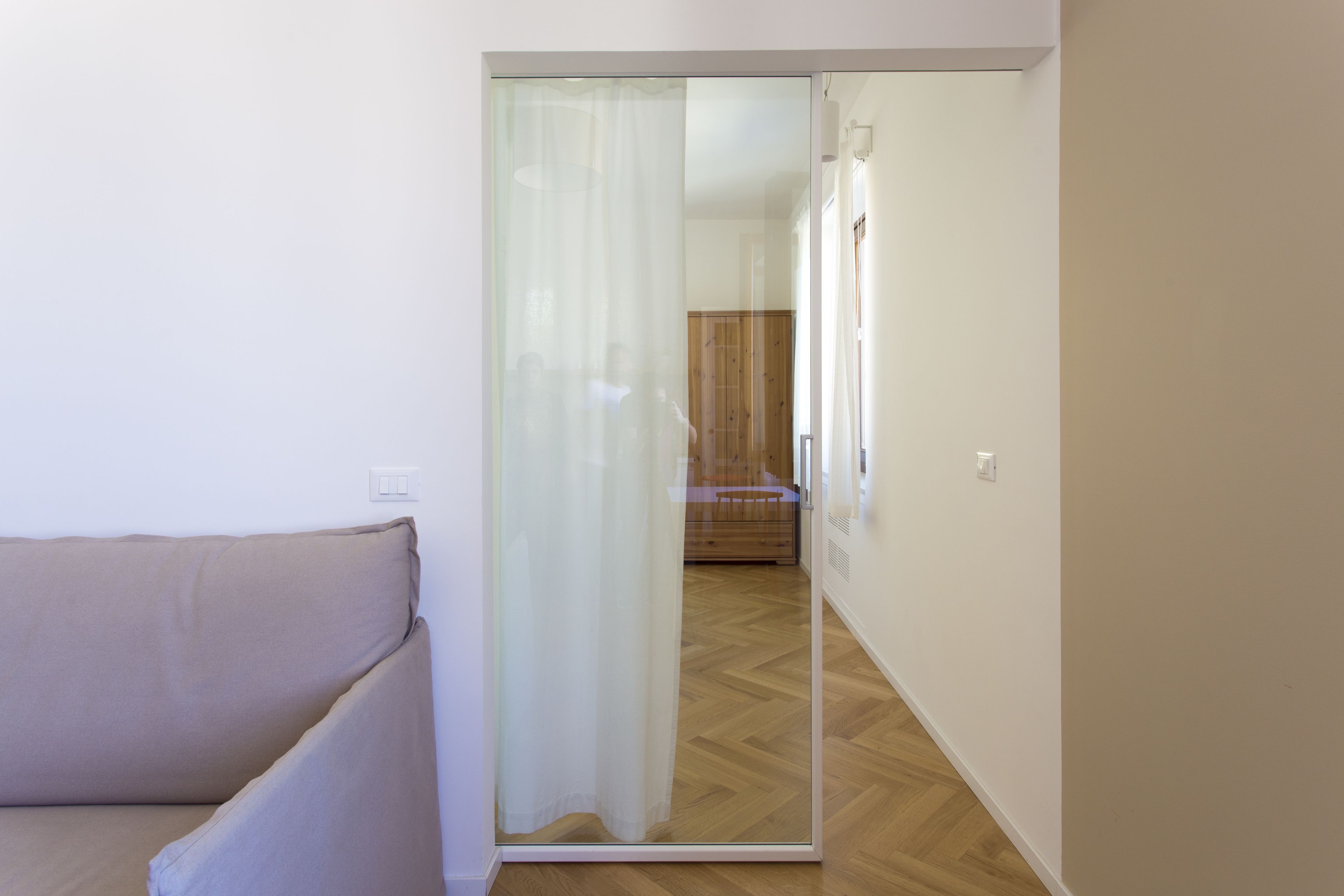 A room with a sliding glass door leading to a wooden floor and a bed.