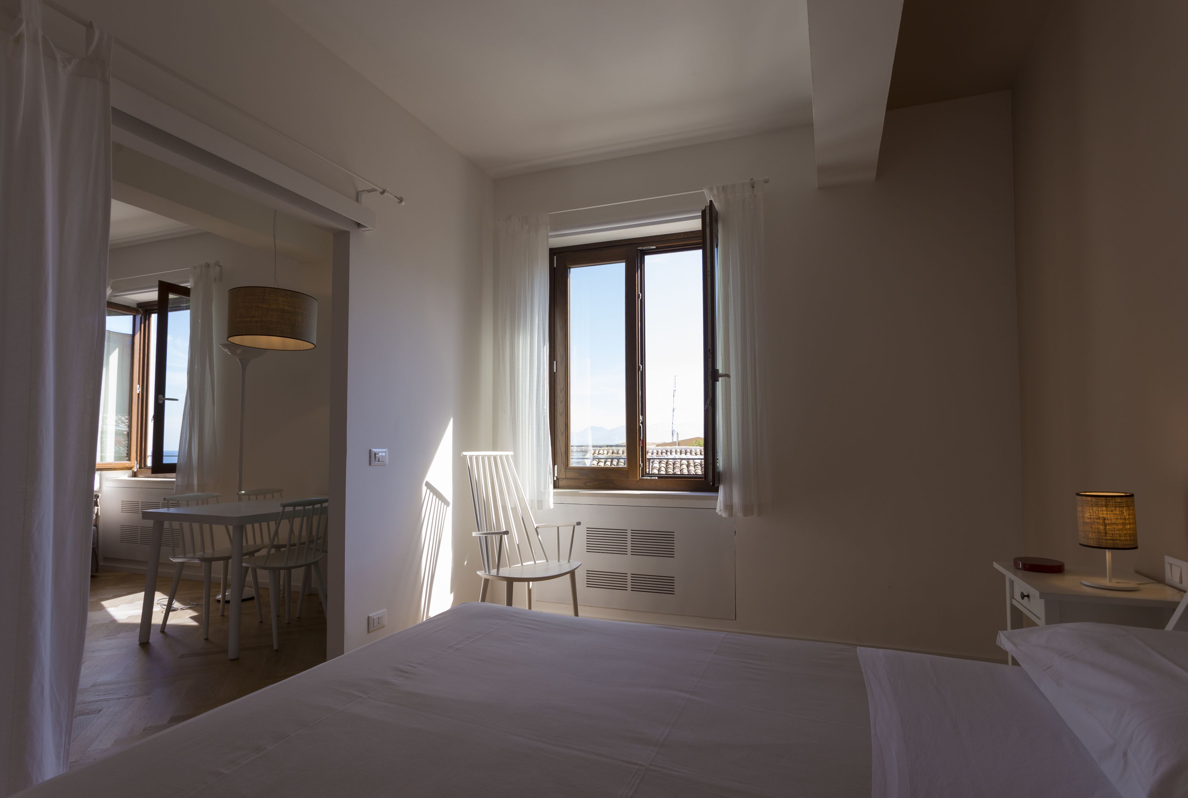 Un dormitorio con cama, escritorio con silla, ventana con vistas y mesita de noche con lámpara.