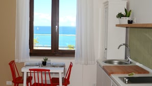 A kitchen with a view of the sea, a dining area with red chairs, and a small plant on the counter. - Residence ITACA (Castellammare del Golfo)
