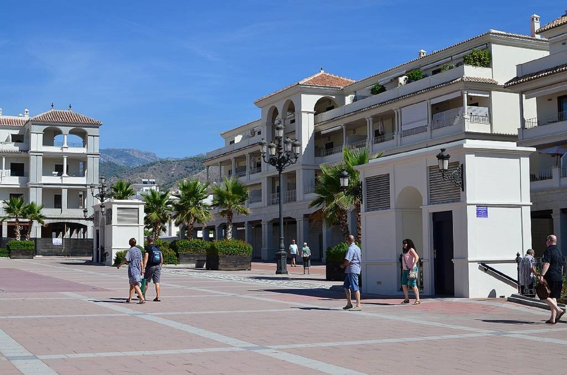 A spacious public square with a central fountain, surrounded by multi-story buildings with balconies and outdoor seating areas.