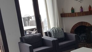 A living room with a sofa, a coffee table, a fireplace, and a view through a sliding glass door. - El Capistrano, Nerja 2 bedroom apartment with south facing private garden (Nerja (Malaga))
