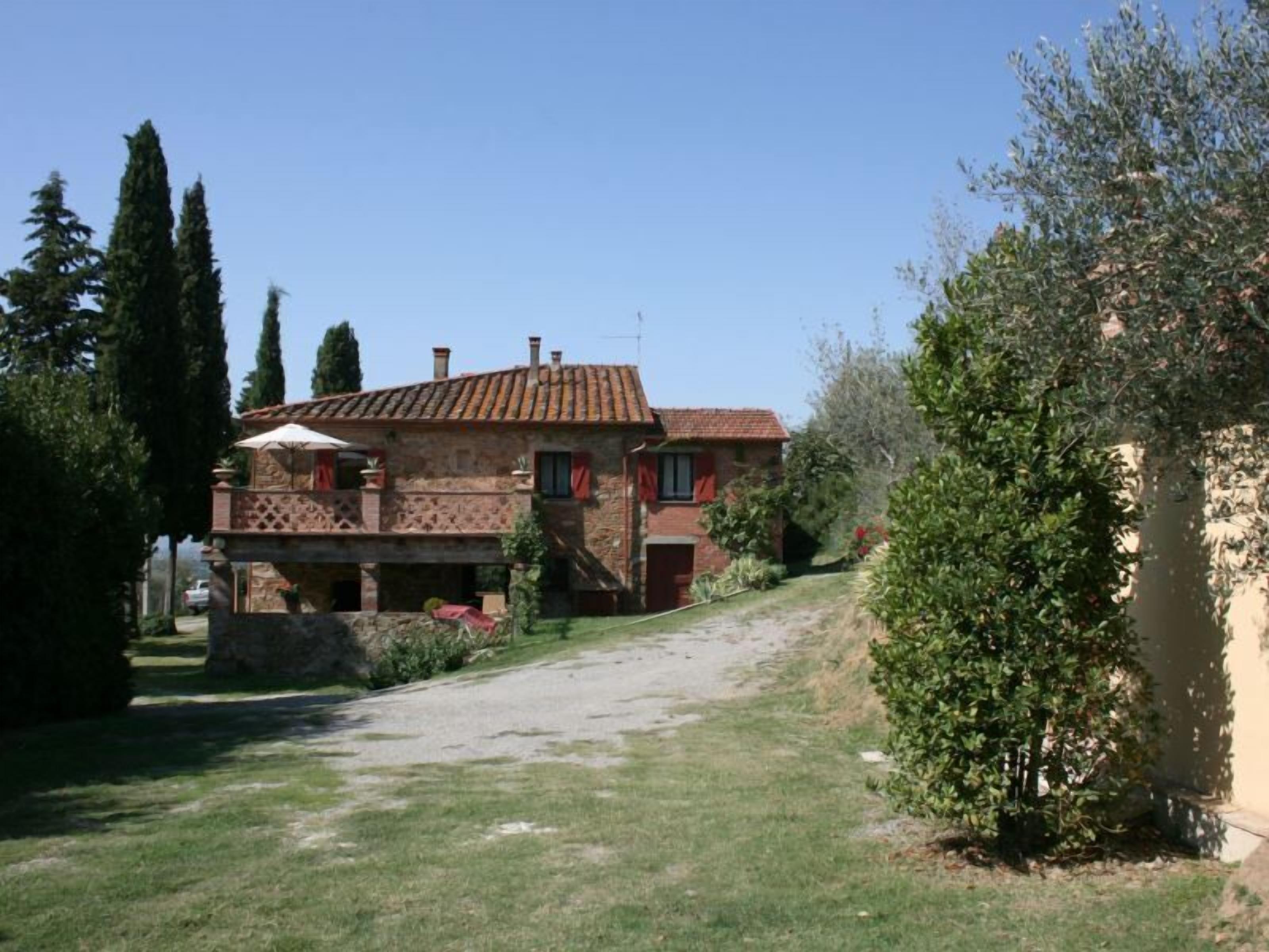 A stone house with a tiled roof, a covered patio, and a garden with trees and shrubs.