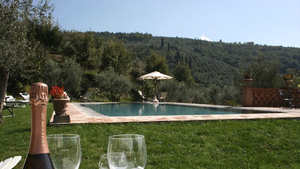 Une scène au bord de la piscine, avec une bouteille et des verres sur un plateau, le tout entouré d’une végétation luxuriante et offrant une vue sur des collines.