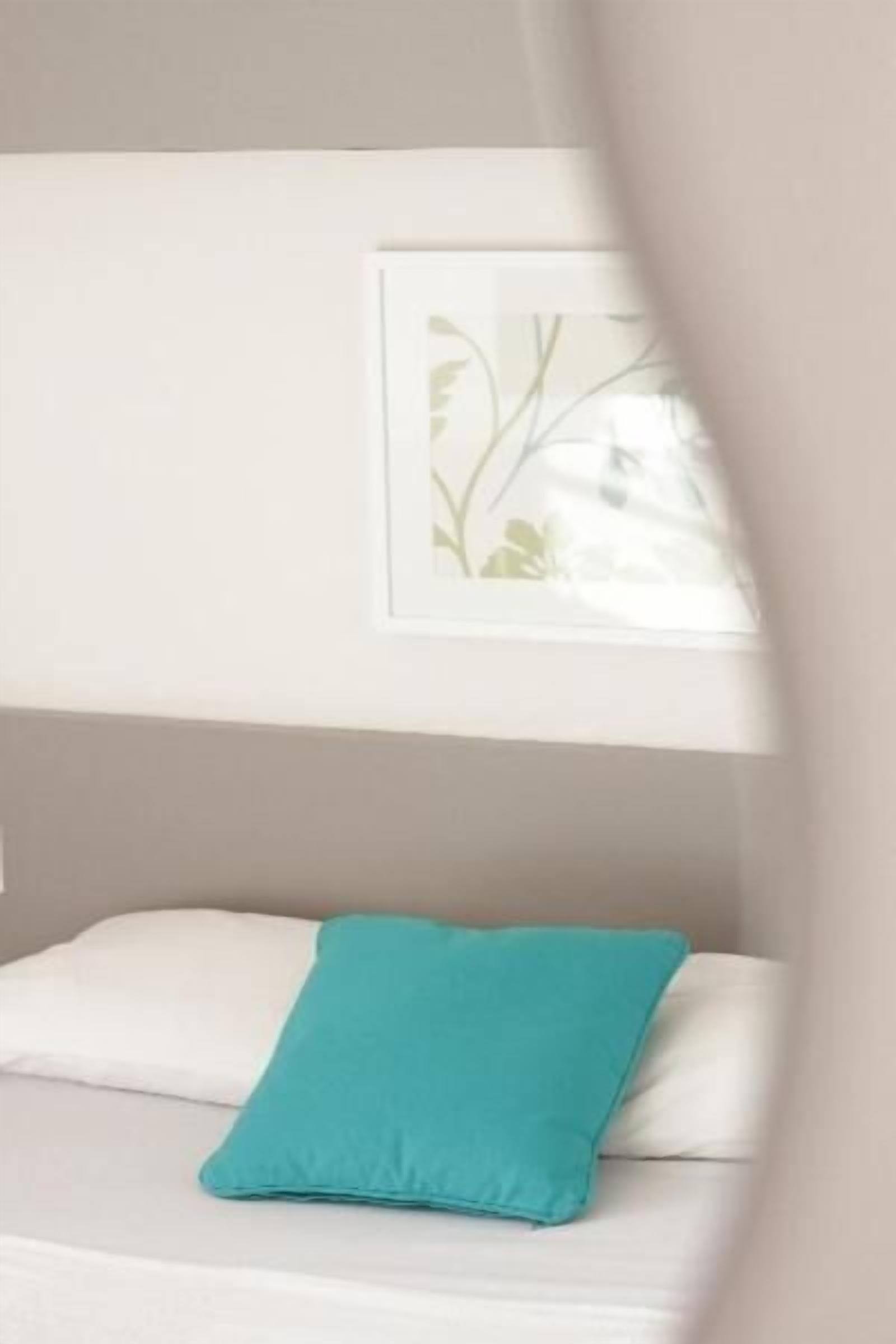A bed with white bedding and a teal pillow.