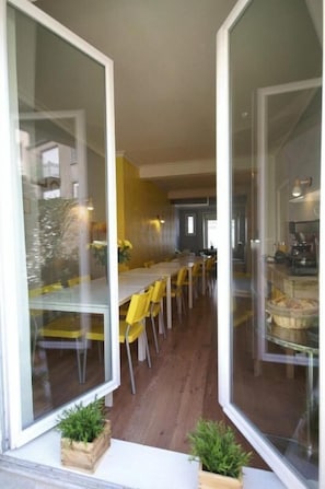 A modern dining area with glass walls, yellow chairs, and a long table. - Hotel Little Lodge (Brest)