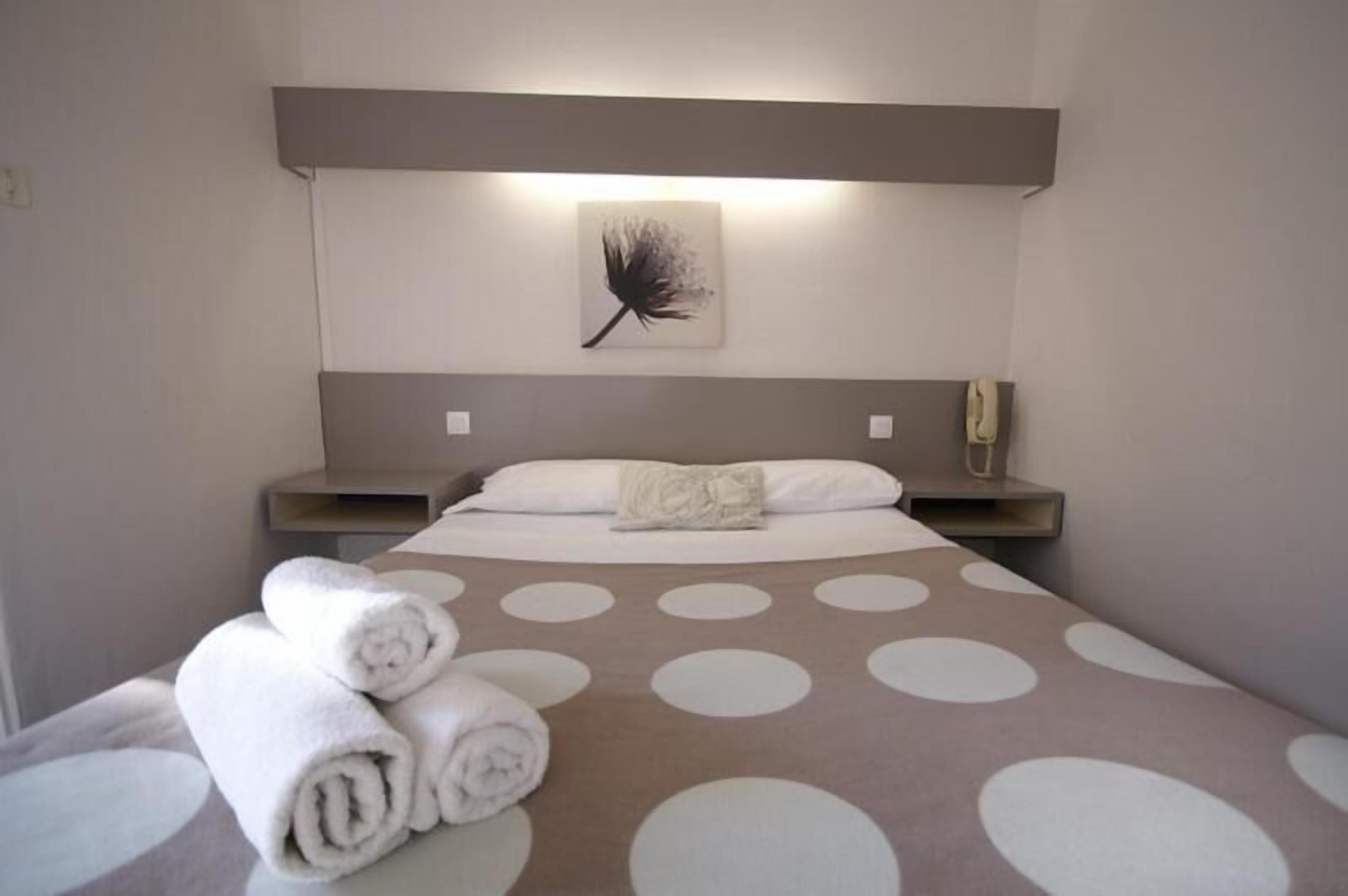 Una habitación de hotel con una cama, una obra de arte en la pared, una mesita de noche y toallas enrolladas.
