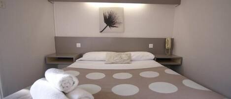 Una habitación de hotel con una cama, una obra de arte en la pared, una mesita de noche y toallas enrolladas.
