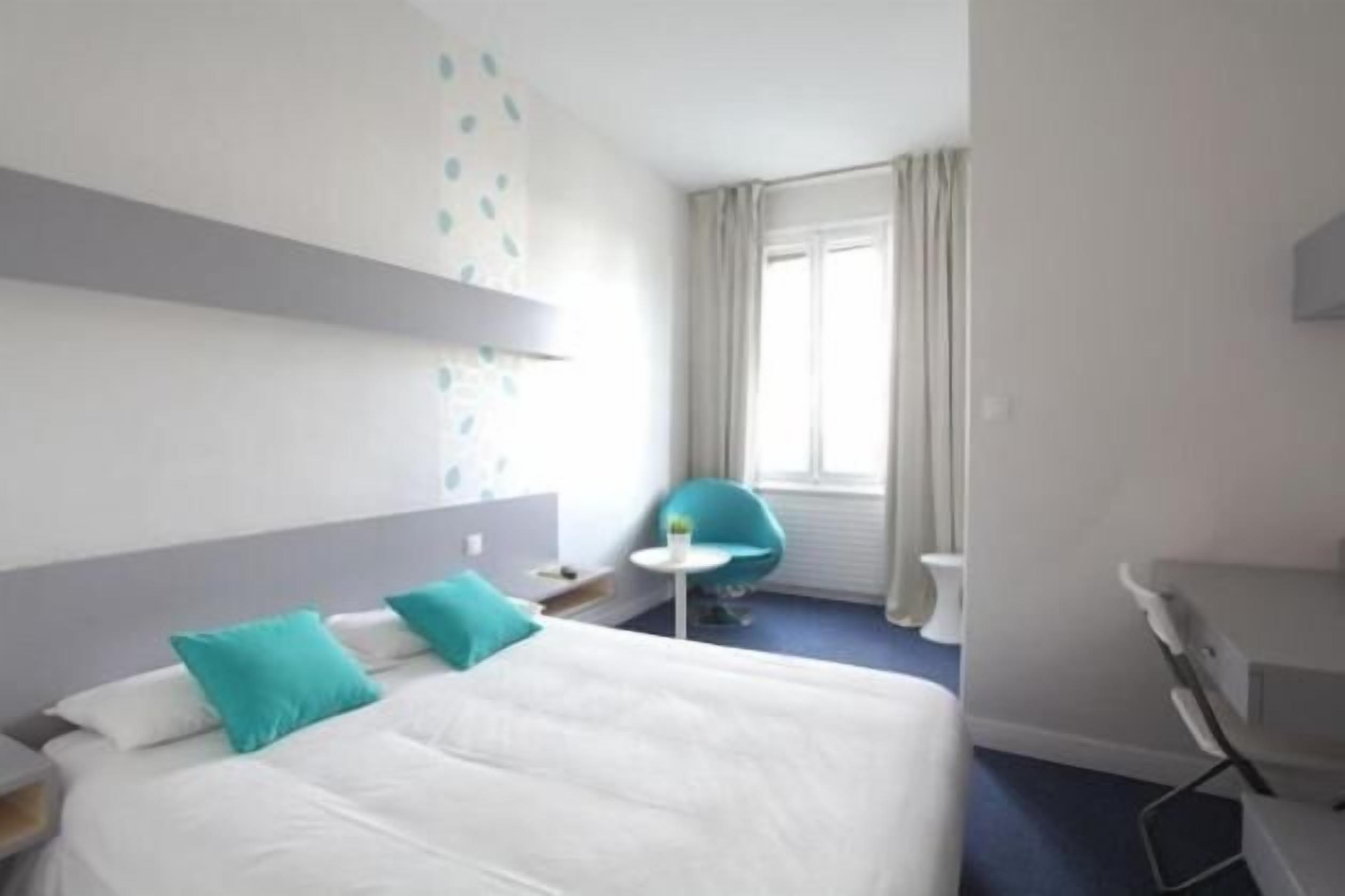 A hotel room with a bed, a desk, a chair, and a small table.