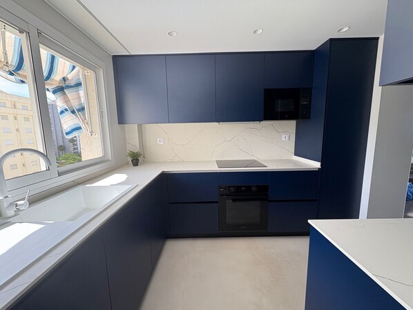 A modern kitchen with dark blue cabinets, a white countertop, a black microwave, and a dishwasher. - Amazing, 5 stars! Beautiful 27m2 terrace beachfront condo! WIFI 150MBS - ONLY FAMILIES (Playa de Gandía)