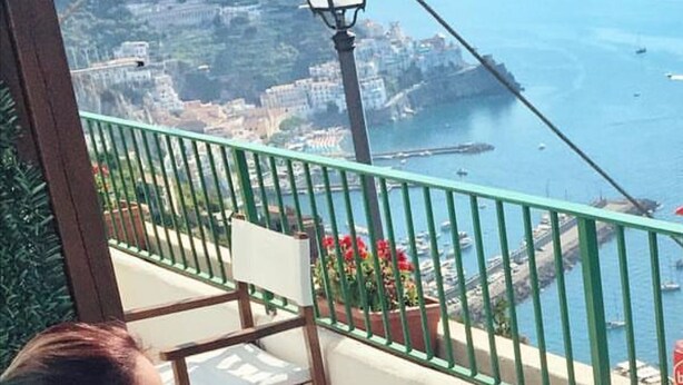 A woman sitting at a table with a view of the sea and mountains. - Residenza Gennaro (Amalfi)