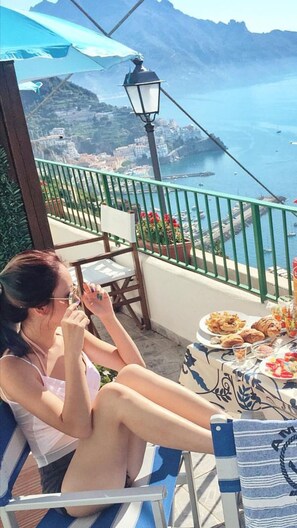 A woman sitting at a table with a view of the sea and mountains. - Residenza Gennaro (Amalfi)