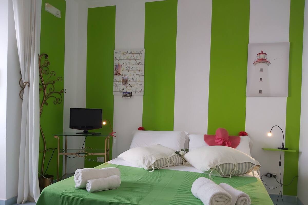 A hotel room with a green-striped wall, a bed with white bedding, a flat-screen TV, and a wall-mounted artwork.