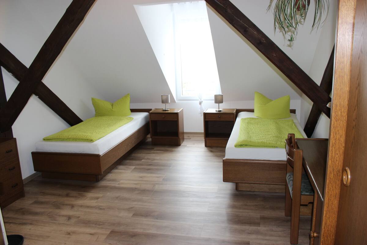 Een kamer met twee bedden, houten vloeren en een schuin dak met zichtbare balken.