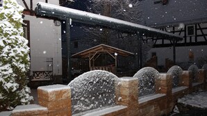 Un espacio exterior cubierto de nieve, con un muro de ladrillo y una estructura de madera al fondo.
