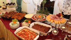 Una mesa de buffet con diversos platos, incluyendo una lasaña grande, una bandeja de salchichas y una variedad de ensaladas y frutas.