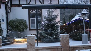 Un espacio exterior cubierto de nieve, con un muro de ladrillo, un árbol de Navidad y una cerca de madera.