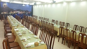 A long dining table set with chairs, a cityscape mural on the wall, and ceiling fans. - Daiichi Cat Ba Hotel (Hai Phong)