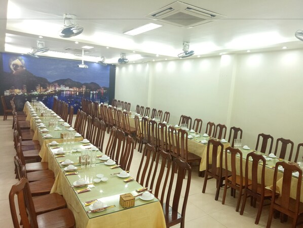 Una larga mesa de comedor con sillas, un mural de un paisaje urbano en la pared y ventiladores de techo.
