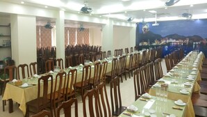 A large banquet hall with long tables set for dining, wooden chairs, and a cityscape mural on the wall. - Daiichi Cat Ba Hotel (Hai Phong)