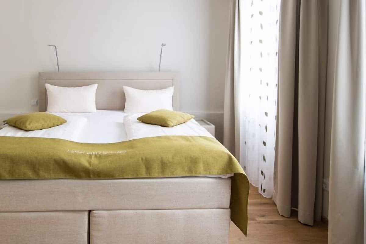 Een netjes opgemaakt bed met een beige hoofdbord, twee witte kussens en een groene plaid.