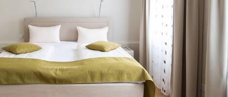 A neatly made bed with a beige headboard, two white pillows, and a green throw blanket.
