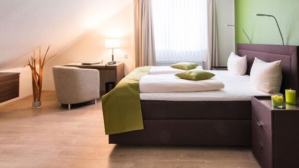 A hotel room with a bed, bedside tables, a lamp, a chair, and a window with curtains. - Hotel am Herkules - garni (Kassel)