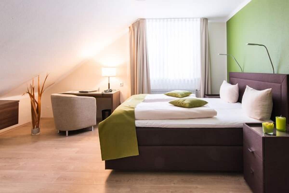 Een hotelkamer met een bed, nachtkastjes, een lamp, een stoel en een raam met gordijnen.