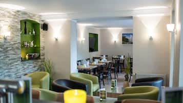 A modern dining area with green and yellow chairs, a stone wall, and a view of the dining room.