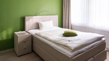 Un dormitorio con cama, mesita de noche y ventana con cortinas.