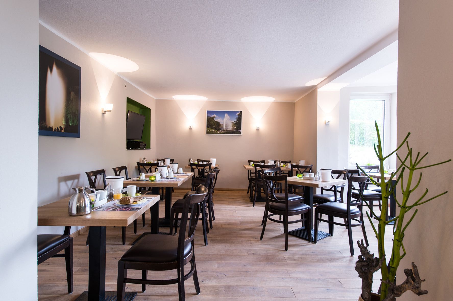 Un espace repas comprenant plusieurs tables et chaises, des luminaires fixés au mur et des œuvres d’art encadrées.