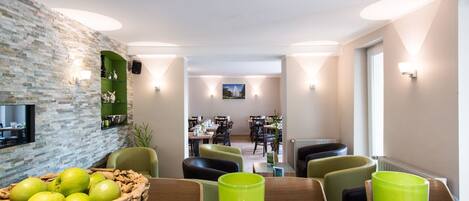 A modern dining area with a stone wall, green chairs, and a table with a fruit basket and green drinks.