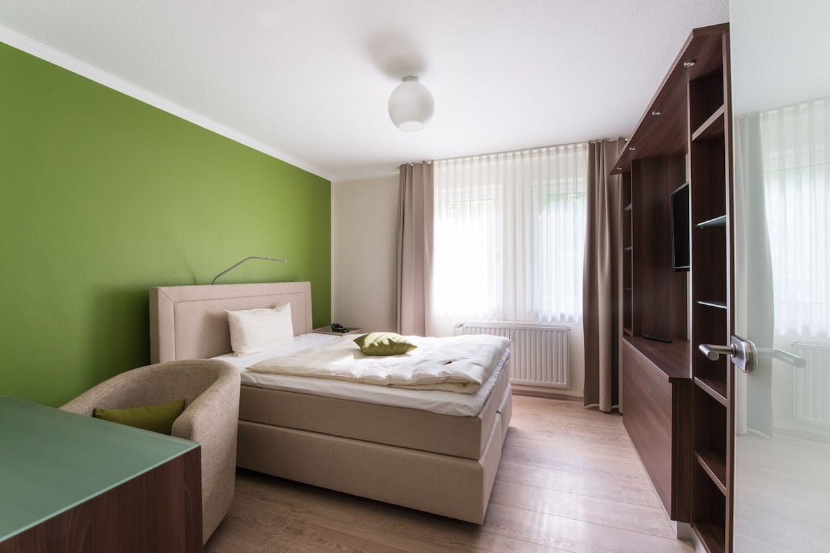 Een slaapkamer met een bed, een bureau, een stoel, een kledingkast en een raam met gordijnen.