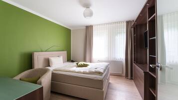 Quarto com cama, escrivaninha, cadeira, guarda-roupa e janela com cortinas.