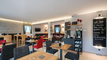 A modern restaurant with wooden tables and chairs, a chalkboard menu, and shelves with wine glasses and bottles.