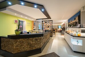 A hotel reception area with a reception desk, a reception sign, a potted plant, a wall-mounted clock, and a framed picture. - Biohotel Wilhelmshöher Tor (Kassel)