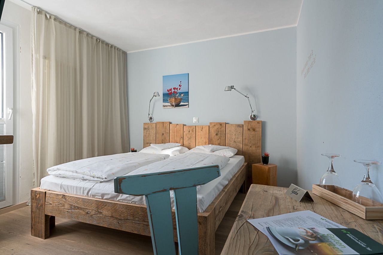 Een slaapkamer met een houten bed, nachtkastje, lamp en raam met gordijnen.