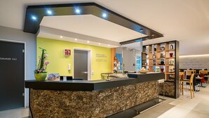 A reception area with a stone counter, a reception desk, a plant, and a bookshelf with various items. - Biohotel Wilhelmshöher Tor (Kassel)