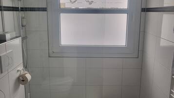 A small, modern bathroom with a toilet, a shower, and a window.