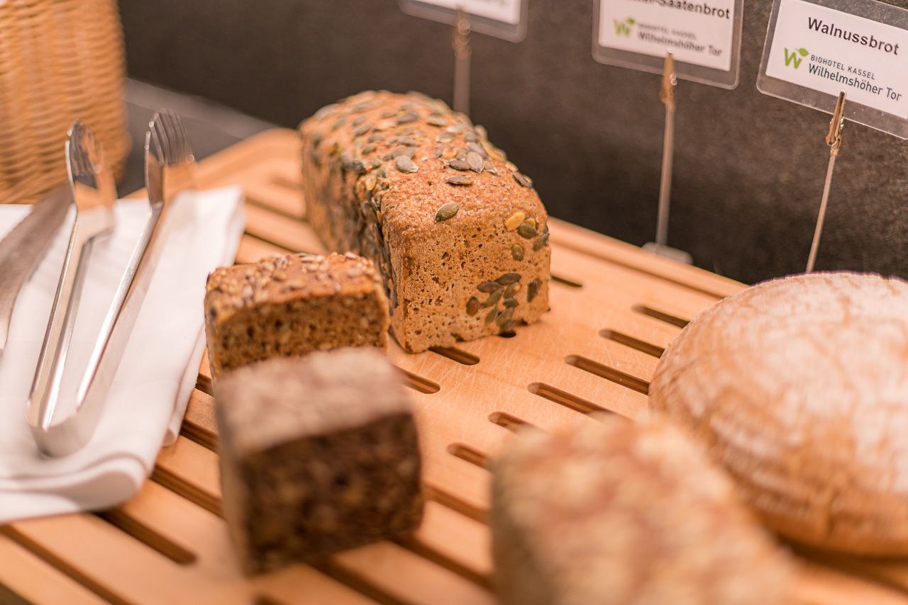 Verschiedene Brotsorten werden auf einer Holzbrett präsentiert, mit Schildern, die die jeweiligen Sorten kennzeichnen.