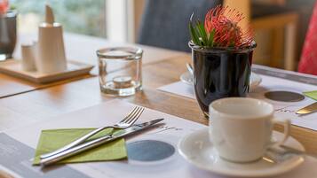 Une table à manger dressée avec une tasse blanche, une soucoupe et des couverts, le tout posé sur un set de table.