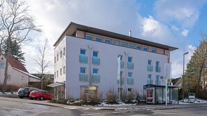 A modern building with a flat roof, multiple windows, and a bus stop shelter. - Biohotel Wilhelmshöher Tor (Kassel)