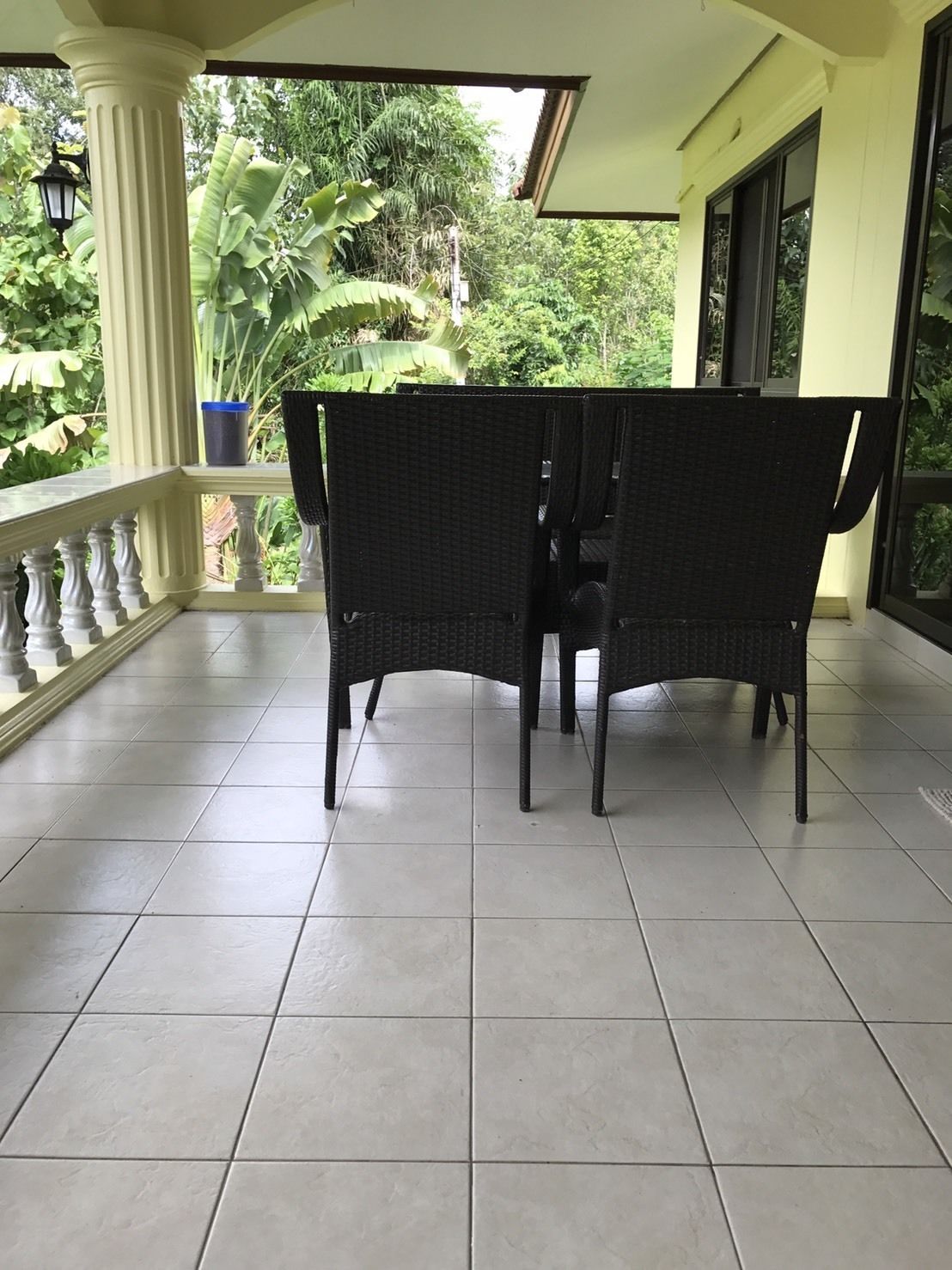 A covered balcony with two wicker chairs, a potted plant, and a view of lush greenery.