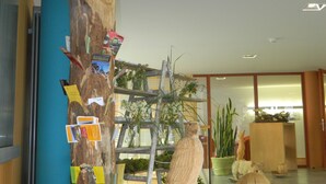 Un vestíbulo con una gran escultura de árbol de madera, una escultura de pájaro y una escalera que lleva a un estante con plantas.