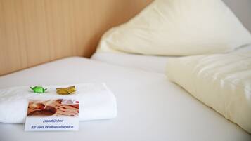 Een net opgemaakt bed met een wit kussen en een opgevouwen handdoek, met een kaartje erop.