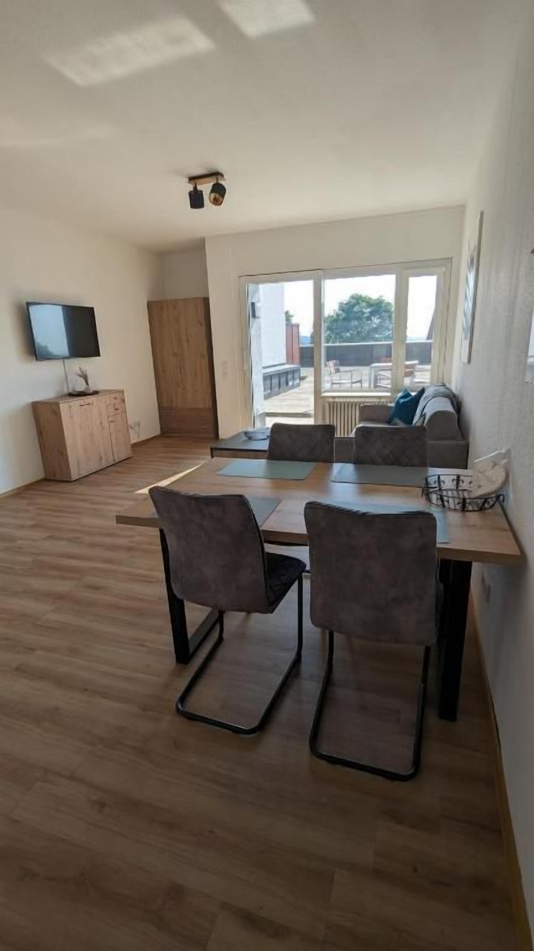 A modern living room with a dining area, a TV on a cabinet, and a large window with a view.