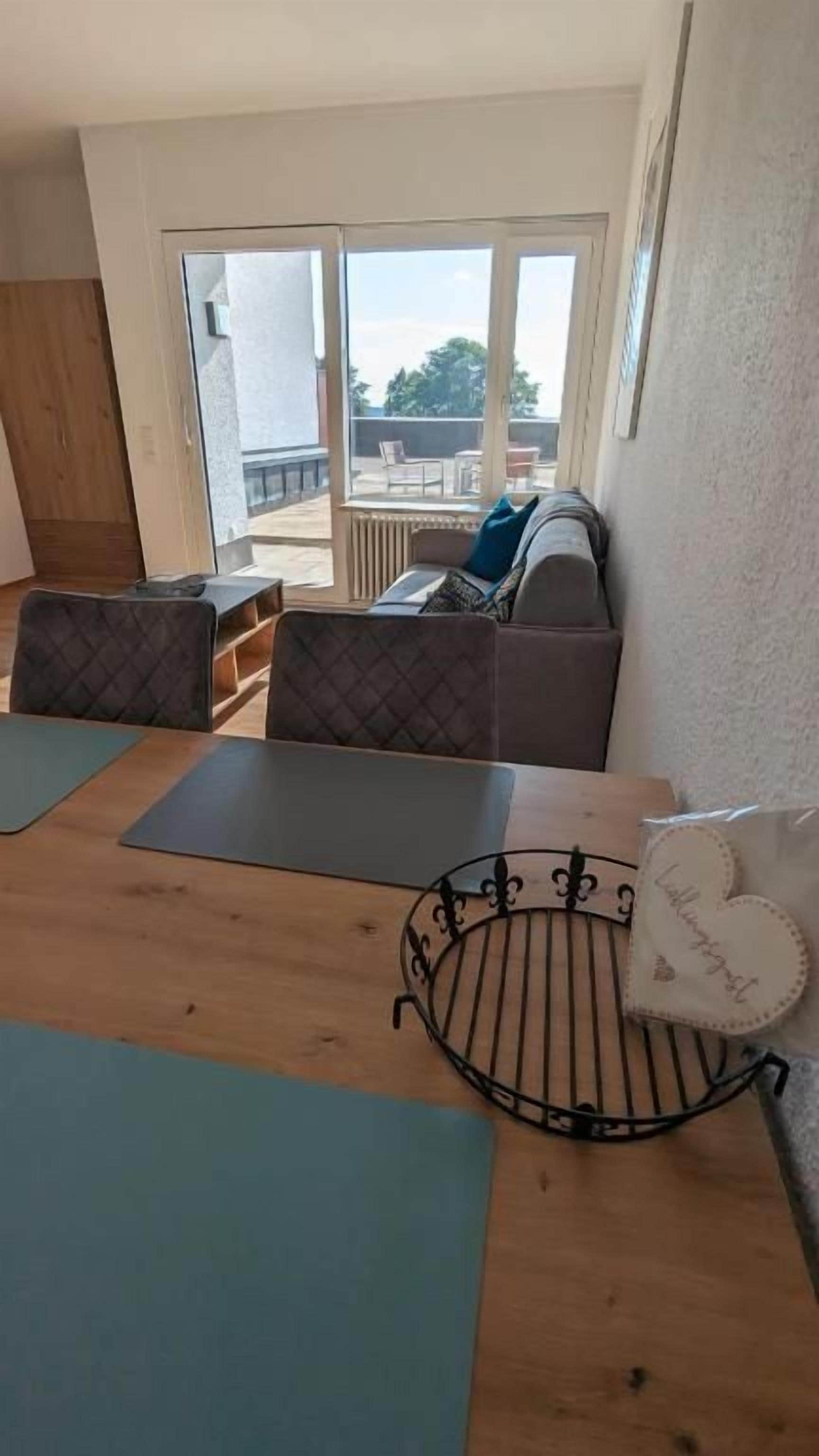 A room with a wooden table, cushioned seating, and a view through a glass door to an outdoor area.