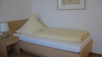 Un lit simple avec un cadre en bois, une table de chevet avec une lampe et un tableau encadré au mur.