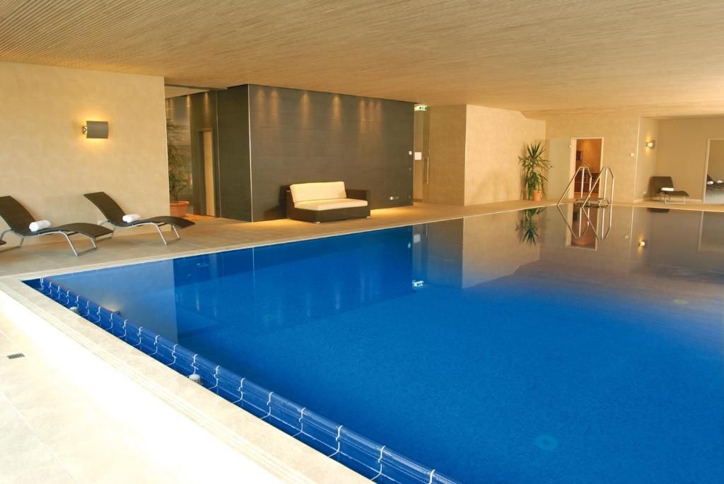 Una piscina interior con sillas de descanso, un sofá y una escalera.