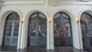 A hallway with three dark wooden doors with intricate designs and light fixtures above them.